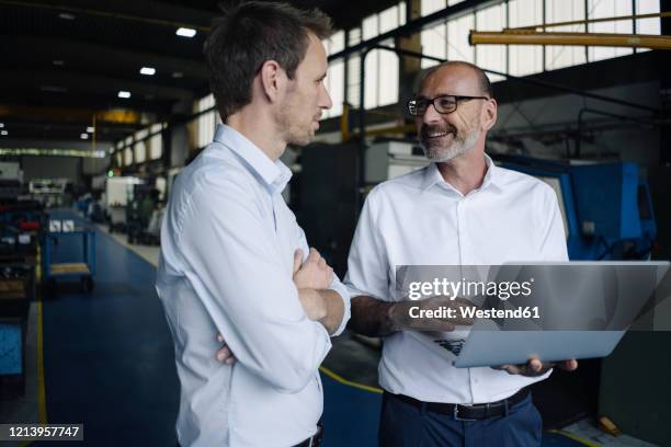 two men using laptop in a factory - team industrie stock-fotos und bilder