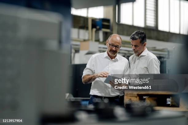 two businessmen using tablet in a factory - herstellendes gewerbe stock-fotos und bilder