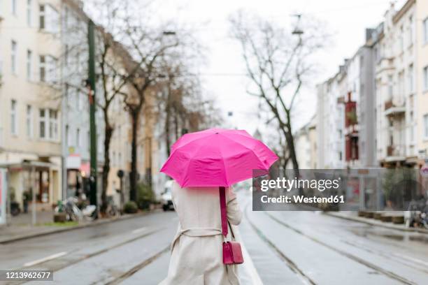 rear view of a woman with pink umbrella walking on street - abrigo rosa fotografías e imágenes de stock