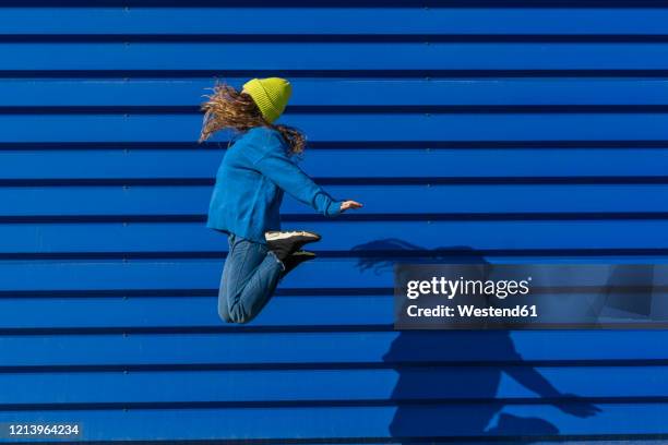 teenage girl jumping in the air in front of blue background - girl jumping stockfoto's en -beelden