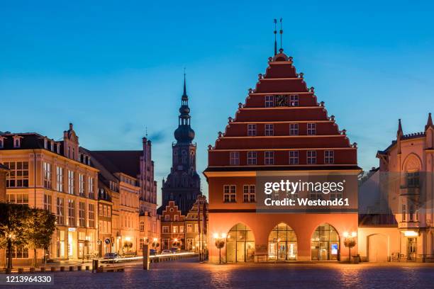 germany,mecklenburg-westernpomerania, greifswald, illuminated town hall at dusk with tower of saint nikolai in background - greifswald stock-fotos und bilder