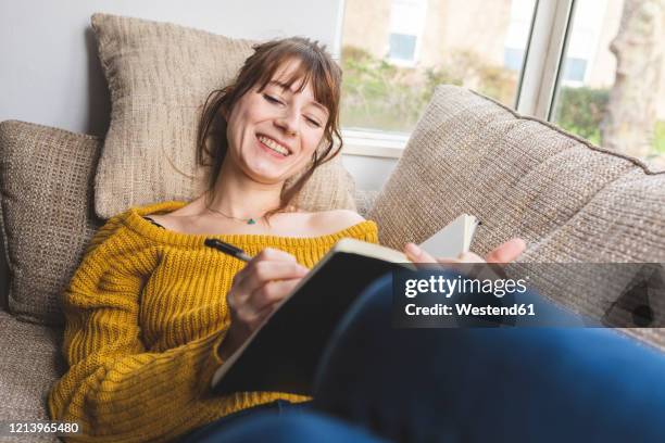 portrait of happy woman lying on couch drawing in sketchbook - bending over backwards stock pictures, royalty-free photos & images