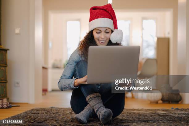 woman with santa hat looking for presents online, using laptop - weihnachten laptop stock-fotos und bilder