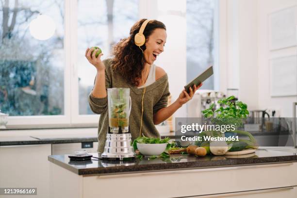 fit woman standing in kitchen, preparing healthy smoothie, using online recipe - smoothie and woman stockfoto's en -beelden