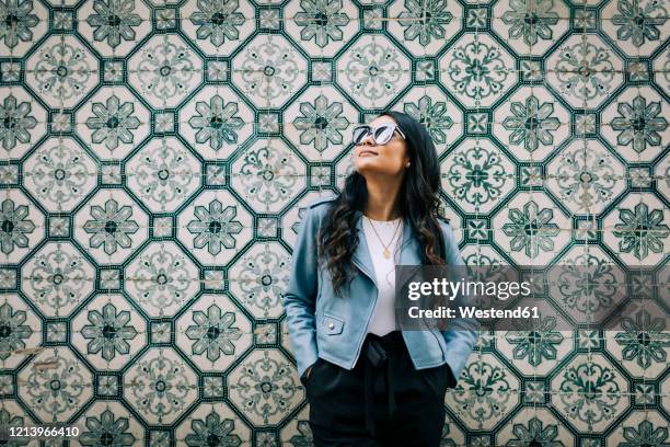 portrait of young woman wearing light blue leather jacket and sunglasses in front of azulejo wall, lisbon, portugal - portugal tile stock pictures, royalty-free photos & images