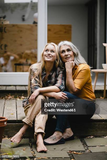 smiling mother and adult daughter sitting on terrace - daughter stock-fotos und bilder