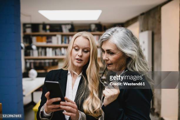 mature and young businesswoman using smartphone in loft office - successor stockfoto's en -beelden