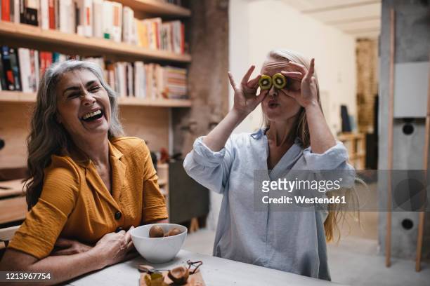 playful young woman with mother covering her eyes with kiwis - 2 people playing joke imagens e fotografias de stock