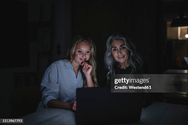 mother and adult daughter looking at laptop on table in the dark - daughters of darkness - fotografias e filmes do acervo