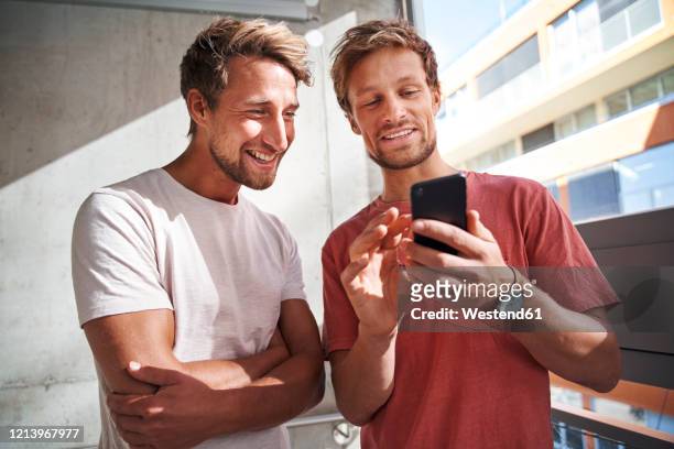 two happy young men sharing smartphone - mann lachen stock-fotos und bilder