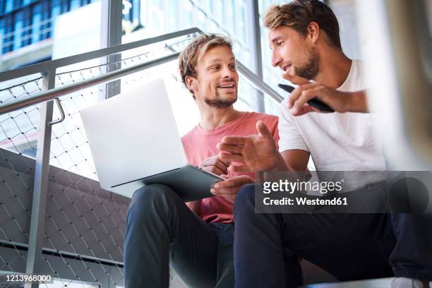 two casual young men sitting on stairs using laptop - founder stock pictures, royalty-free photos & images