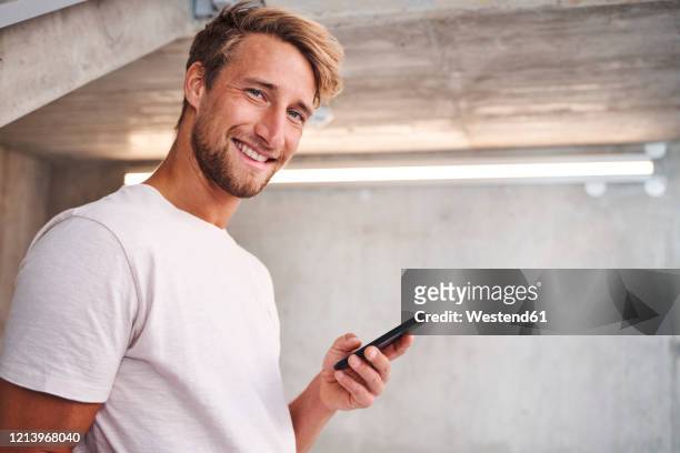 portrait of attactive young man wearing white t-shirt holding smartphone - solo un uomo giovane foto e immagini stock
