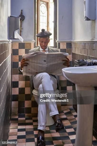 stylish young businessman with a beret reading the newspaper sitting in the restroom - bad news stock-fotos und bilder