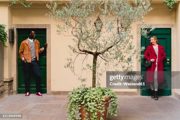 smiling young man and woman standing at front doors in patio looking at each other - neighbour stock pictures, royalty-free photos & images