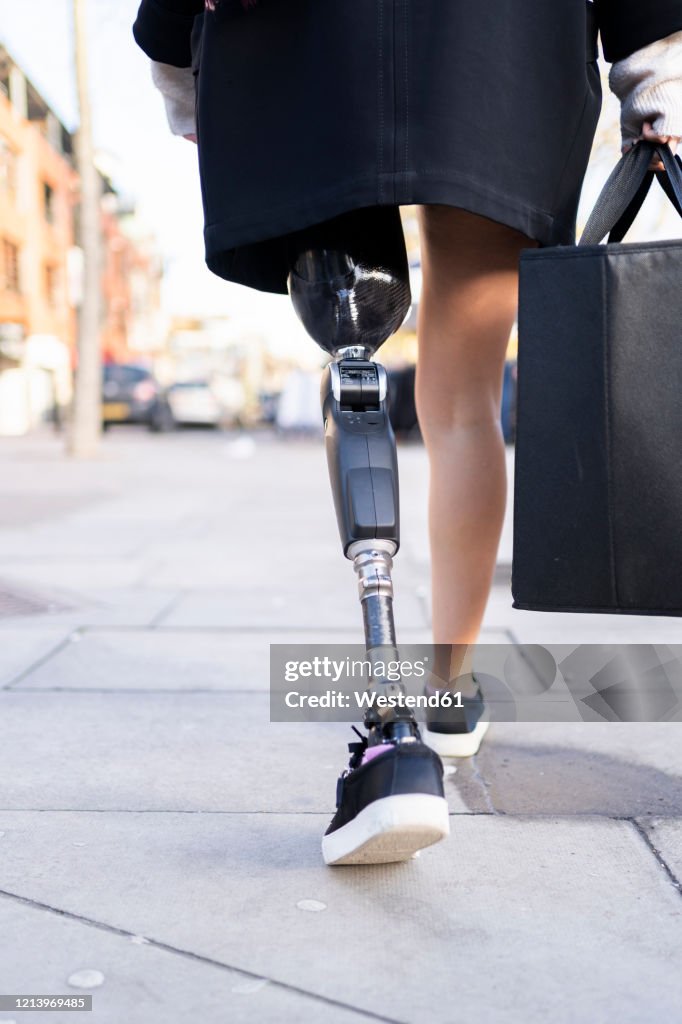 Low section of woman with leg prosthesis walking in the city