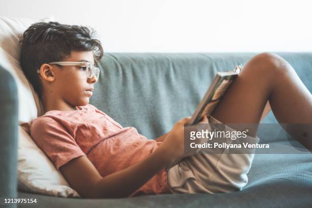 boy reading book on sofa - reading imagens e fotografias de stock