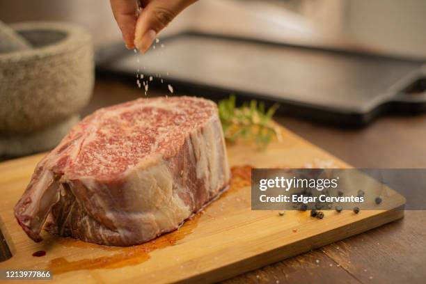 bone-in rib eye steak being salted - himalayan salt stock-fotos und bilder