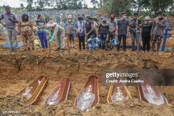 People wearing protective masks observe to the graves with the remains of their relatives during a mass burial of coronavirus pandemic victims at the...