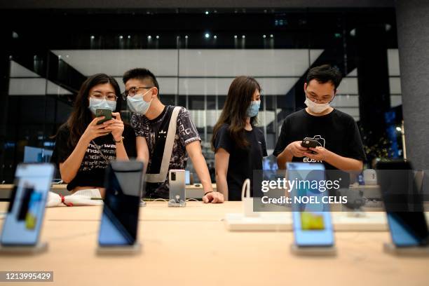 People wearing protective face masks, as a preventive measure against the COVID-19 novel coronavirus, look at smartphones on display at Huawei...