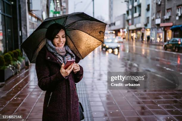 woman using smartphone downtown in rain - rainy weather stock pictures, royalty-free photos & images