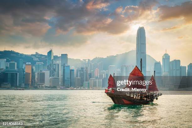 red sail junkboat cruising along hong kong cityscape at sunset - hong kong fotografías e imágenes de stock