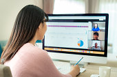Back view of Asian business woman talking to her colleagues about plan in video conference. Multiethnic business team using computer for a online meeting in video call. Group of people smart working from home.