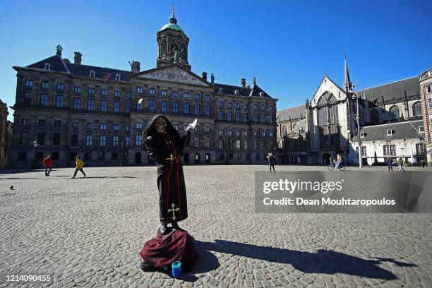 Street perfromer poses in front of Koninklijk Paleis or The Royal Palace Amsterdam which will follow national policy regarding the coronavirus due to...