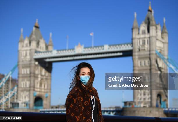 Member of the public poses for a photo in front of Tower Bridge whilst wearing a protective mask on March 22, 2020 in London, England. Coronavirus...