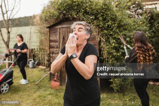adult woman suffering from spring allergy and blowing a runny nose with a tissue while working in the garden - sneeze stock pictures, royalty-free photos & images