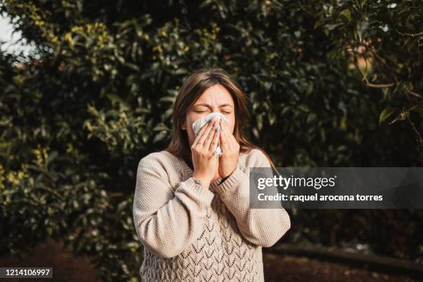 young woman suffering spring allergy and blowing nose with a tissue in the nature - season 1 stock-fotos und bilder