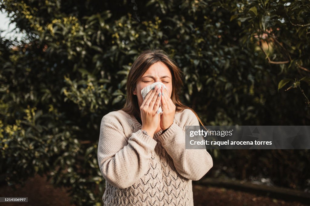 Young woman suffering spring allergy and blowing nose with a tissue in the nature