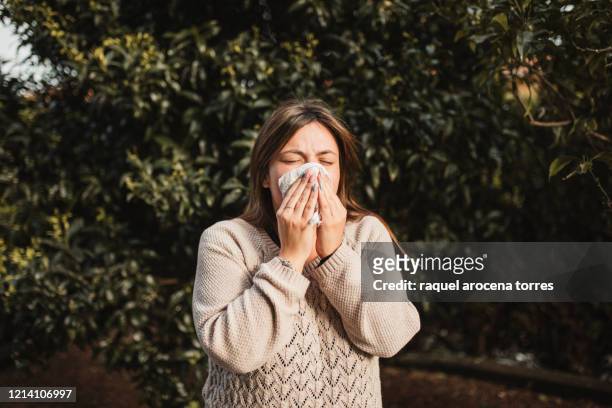 young woman suffering spring allergy and blowing nose with a tissue in the nature - estação do ano - fotografias e filmes do acervo