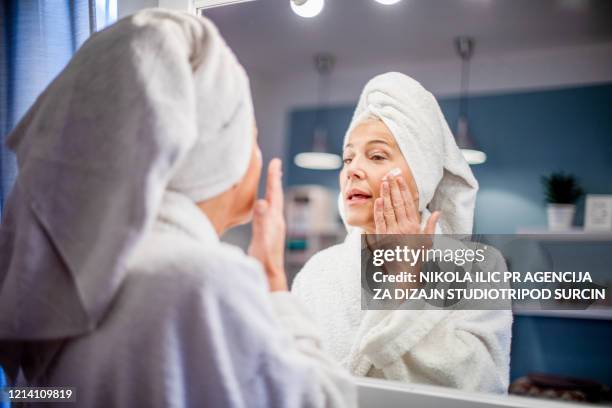 rijpe vrouw die gezichtsroom toepast. - gezichtscrème stockfoto's en -beelden