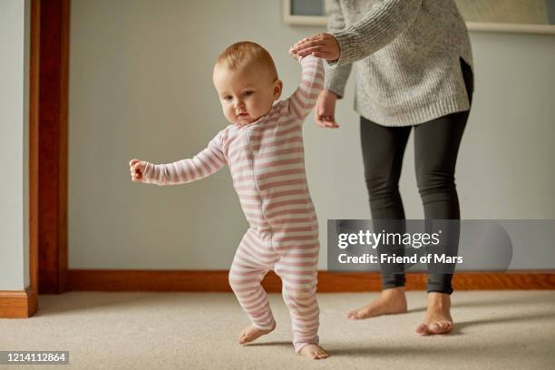 baby holding hands with young adult taking first steps leaning and unsure - första stegen bildbanksfoton och bilder