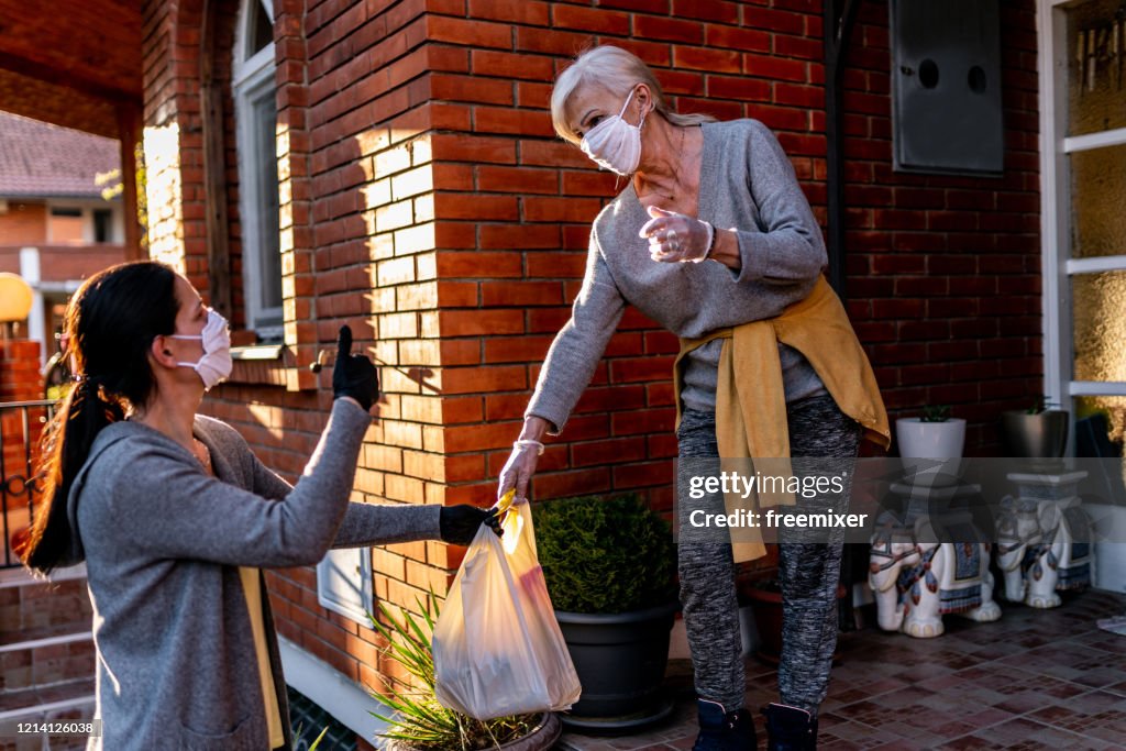 Female volunteer bringing groceries to a senior woman at home