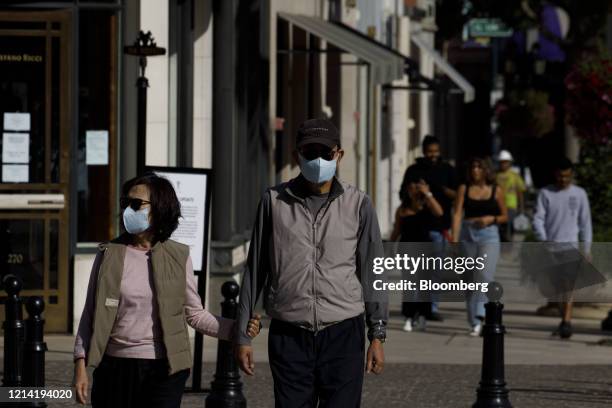 People wear protective masks while walking in front of luxury retail stores on Rodeo Drive in Beverly Hills, California, U.S., on Tuesday, May 19,...