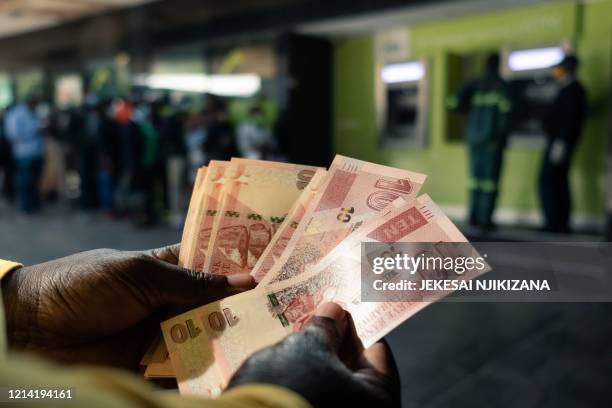 Man counts a wad of the new Zimbabwean ten-dollar notes received from an ATM outside a bank in Harare on May 20, 2020. - The Reserve Bank of Zimbabwe...