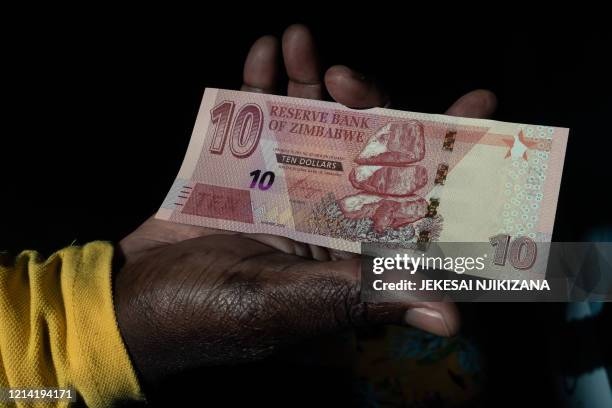 Man shows a wad of the new Zimbabwean ten-dollar notes received from an ATM outside a bank in Harare on May 20, 2020. - The Reserve Bank of Zimbabwe...