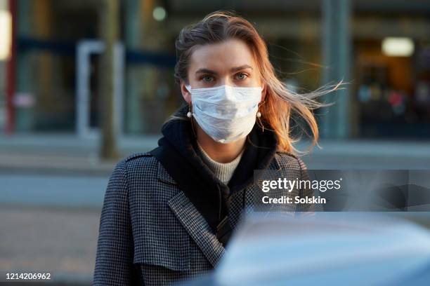 young woman standing on city street wearing protective face mask - griepmasker stockfoto's en -beelden