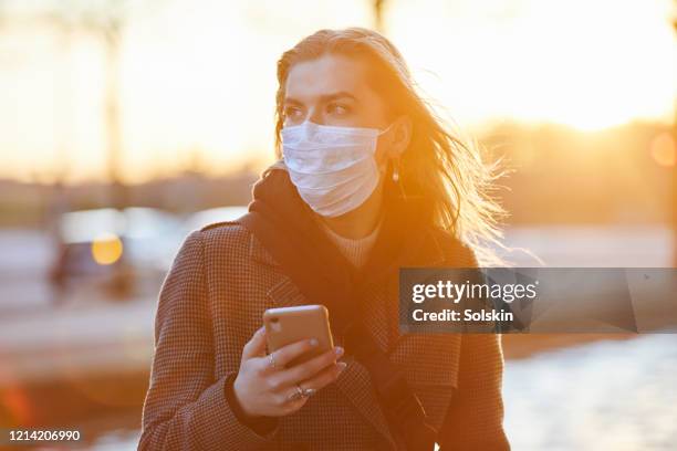 young woman wearing protective face mask using smart phone - commuter mask stock pictures, royalty-free photos & images