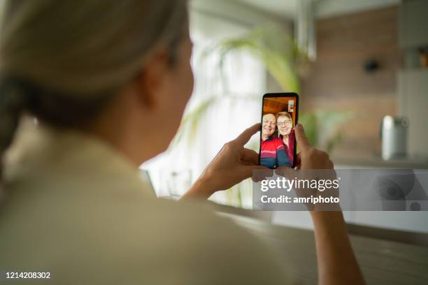 glimlachende hogere volwassen ouders die met dochter over mobiele telefoonvideovraag spreken - family looking at smartphone stockfoto's en -beelden