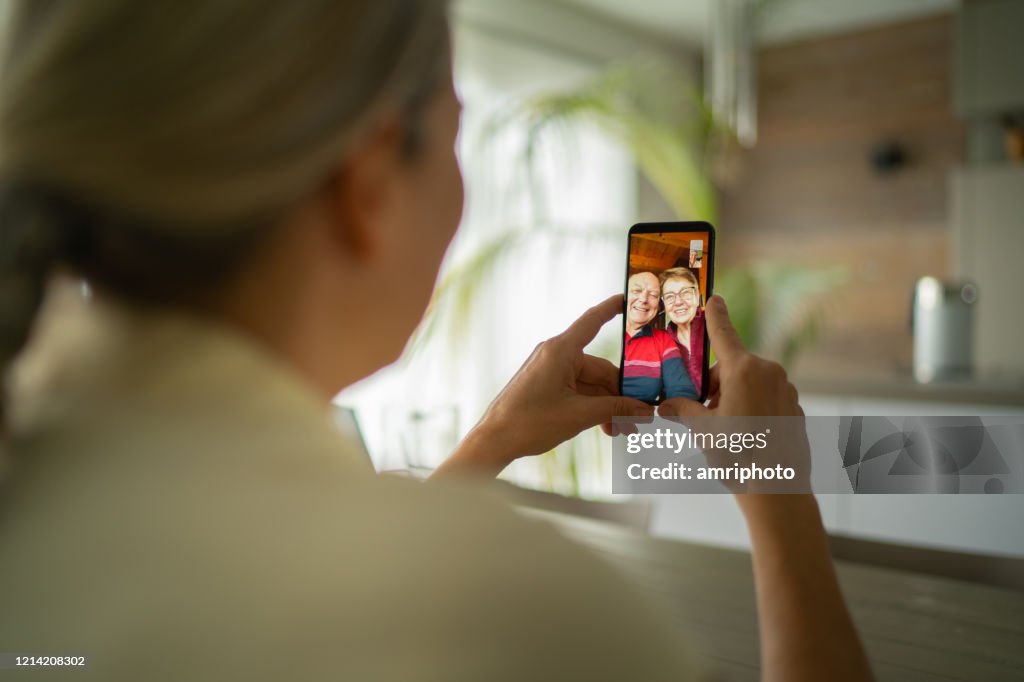 Smiling senior adult parents talking with daughter over mobile phone video call