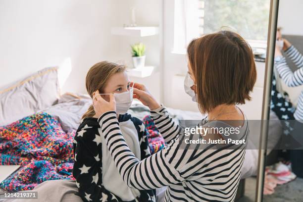 mother putting mask on daughter - pandemic illness stockfoto's en -beelden