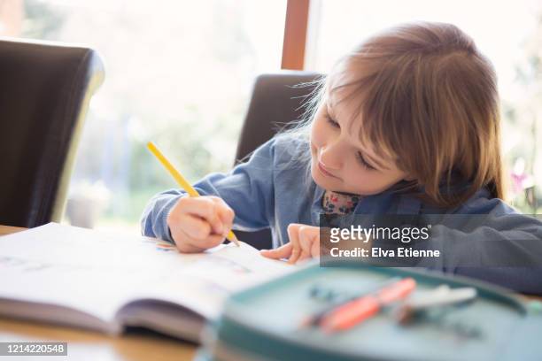 child (6-7) doing school homework at a dining table - fachbuch stock-fotos und bilder