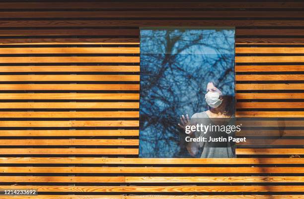 woman with mask looking through window - cladding stockfoto's en -beelden