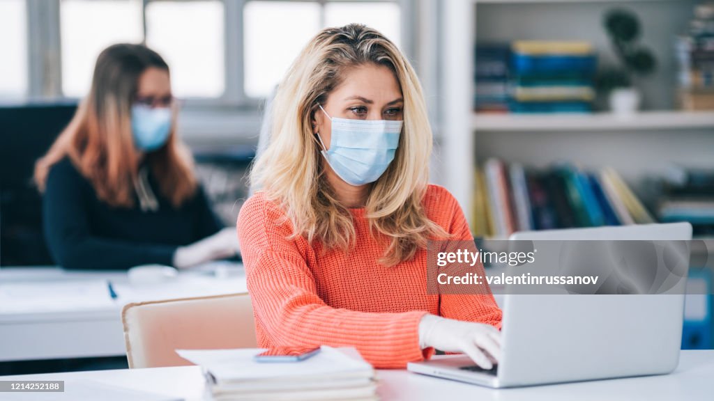 Colleagues in the office working while wearing medical face mask during COVID-19