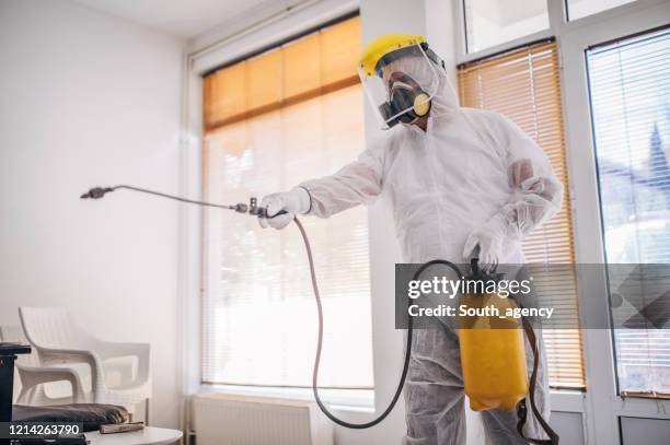 uomo in tuta protettiva che disinfetta e spruzza ogni stanza dell'edificio - diserbante foto e immagini stock