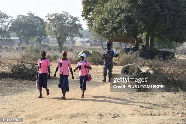 Policeman walk behind school girls as they cross the border in Yemboate, the northern Togo border post with Burkina Faso, on February 17, 2020. -...