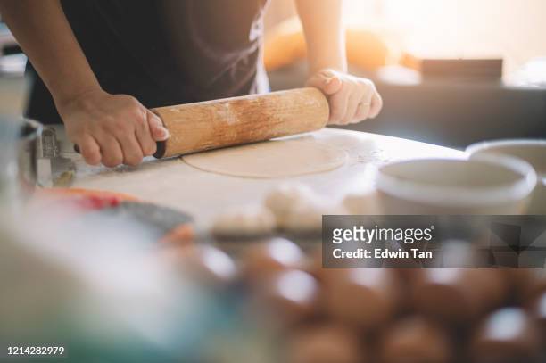 une femme de maison chinoise asiatique préparant la nourriture utilisant le rouleau à pâtisserie avec la farine mélangée avec des oeufs sur la table faisant la pâte - rolling pin photos et images de collection