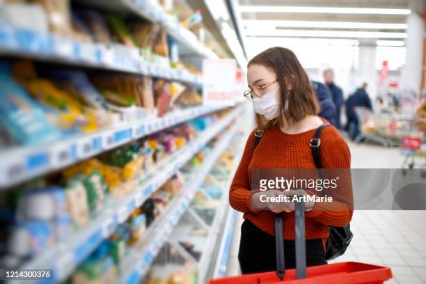 giovane donna che fa la spesa in un negozio di alimentari e indossa una maschera medica protettiva - consumerism foto e immagini stock